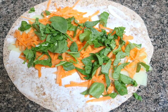 tortilla flat on counter with sliced carrots and spinach on top
