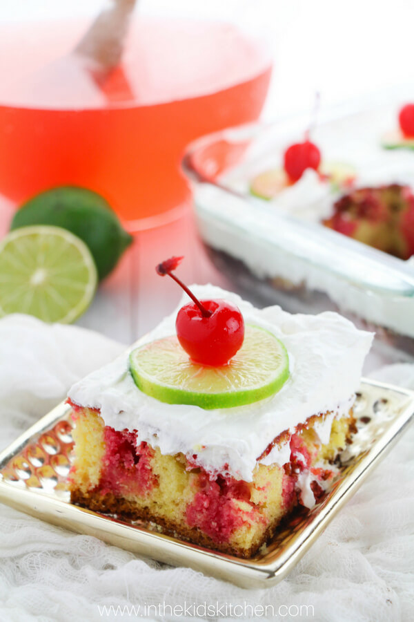 slice of cherry poke cake with whipped topping and fruit on top