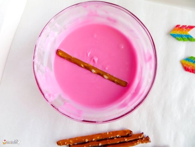 dipping pretzel sticks in melted pink chocolate