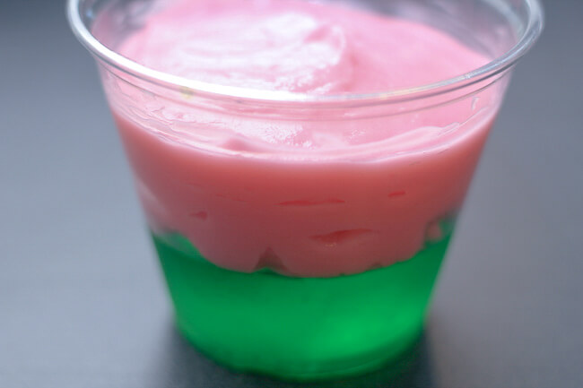  pink pudding layered on top of green jello in a clear cup