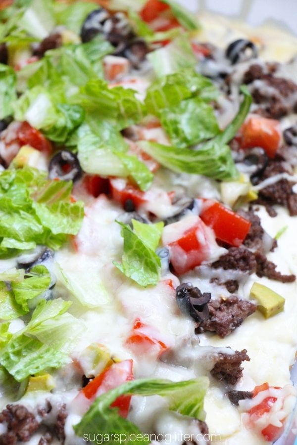 close up on taco pizza toppings: lettuce, ground beef, melted cheese, diced tomatoes