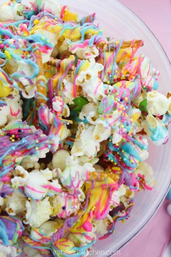 bowl of popcorn topped with colorful melted candy drizzle and sprinkles