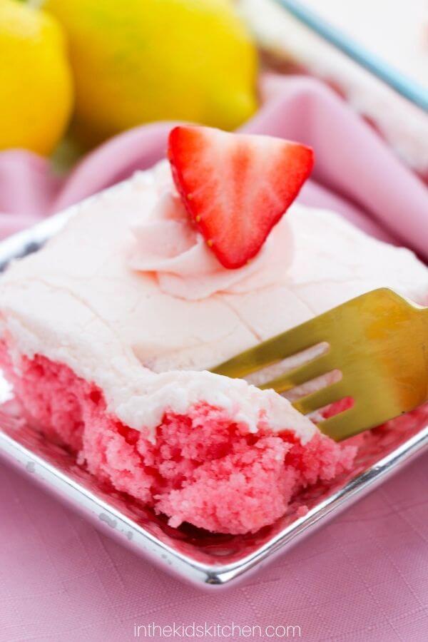 slice of frosted strawberry cake with a strawberry on top