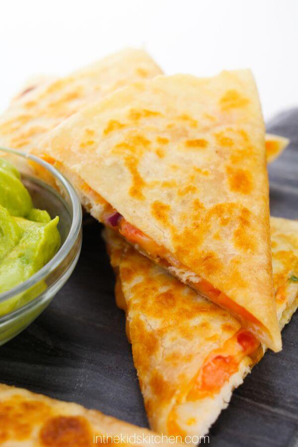 stack of cheesy chicken quesadillas with a side of guacamole