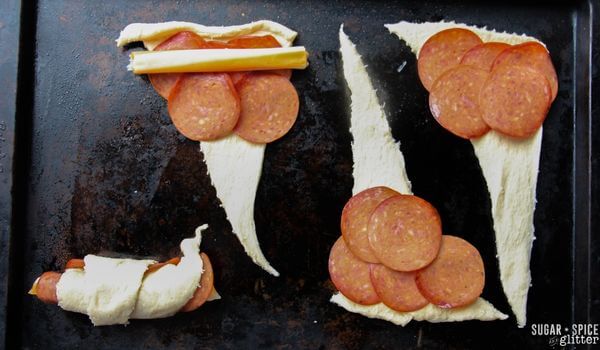 crescent doll unrolled on baking sheet with pepperoni on top.