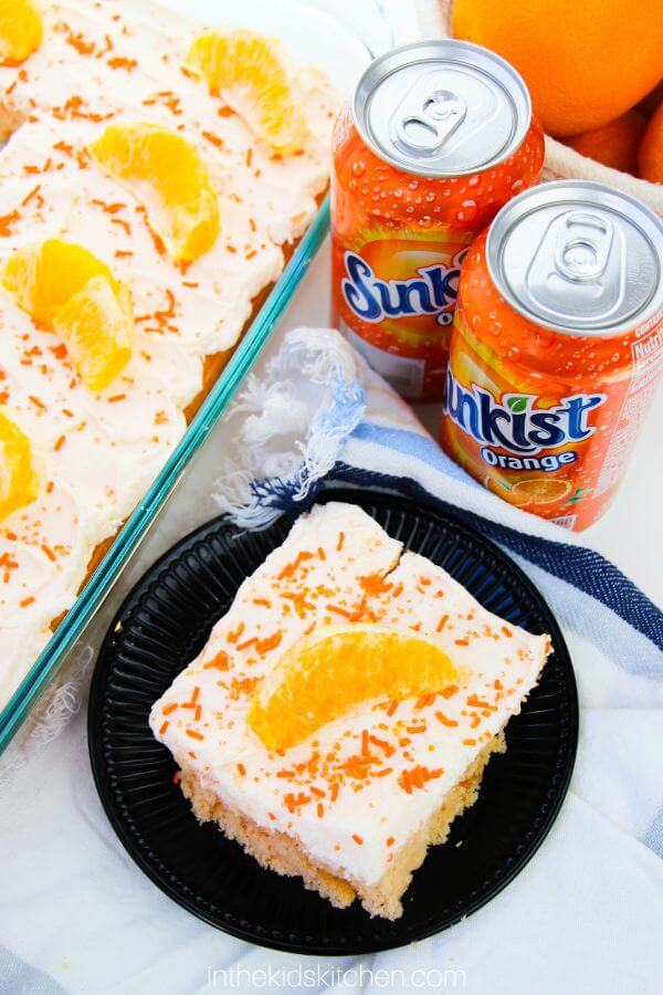 top-down view of a creamsicle cake and cans of orange soda