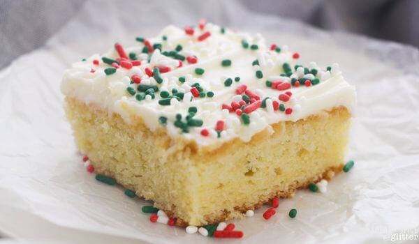slice of sugar cookie cake topped with cream cheese frosting and Christmas sprinkles.