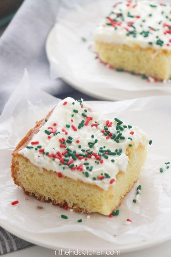 two slices of white sheet cake with cream cheese icing and Christmas sprinkles.