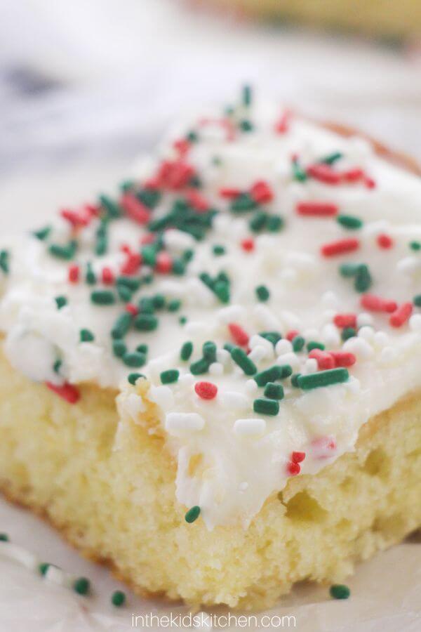 close up of a slice of Christmas sugar cookie cake, with cream cheese icing and holiday sprinkles.