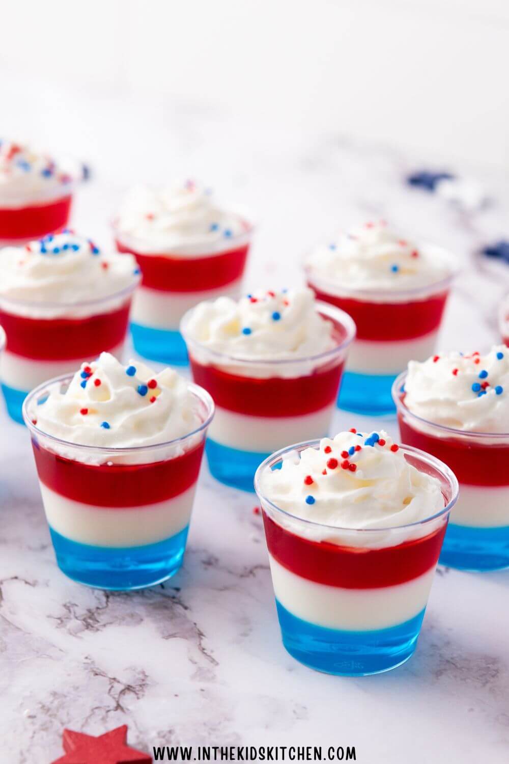 red, white, and blue jello cups topped with whipped cream.